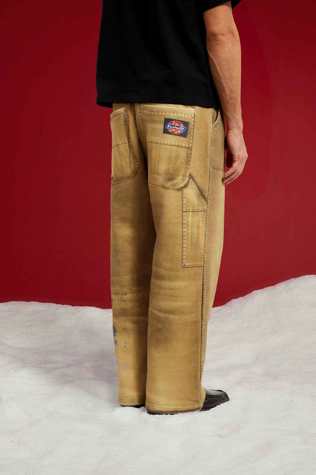 Trompe L'Oeil Printed Double Knee Sweatpants in mustard, printed to look like faded, paint-splattered workwear. Worn on a model, back view from the waist down, with the printed patch pockets and woven work label.