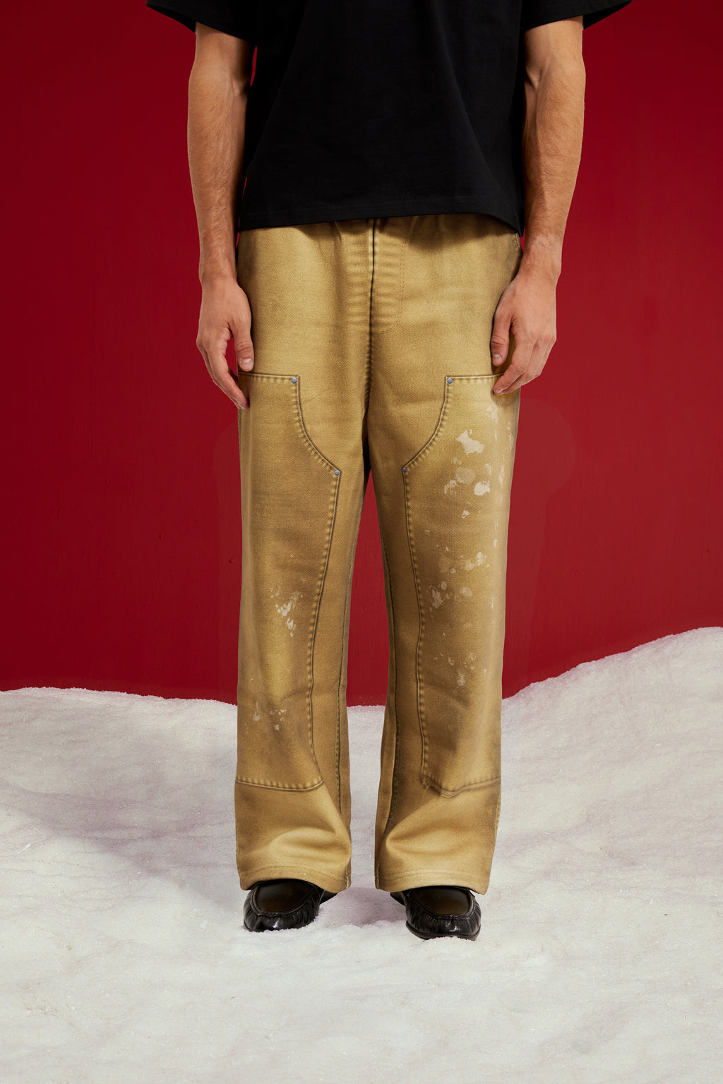 Trompe L'Oeil Printed Double Knee Sweatpants in mustard, printed to look like faded, paint-splattered workwear. Worn on a model, front view from the waist down.