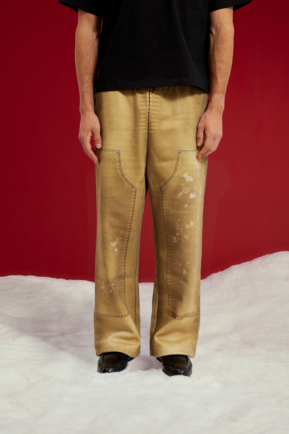 Trompe L'Oeil Printed Double Knee Sweatpants in mustard, printed to look like faded, paint-splattered workwear. Worn on a model, front view from the waist down.