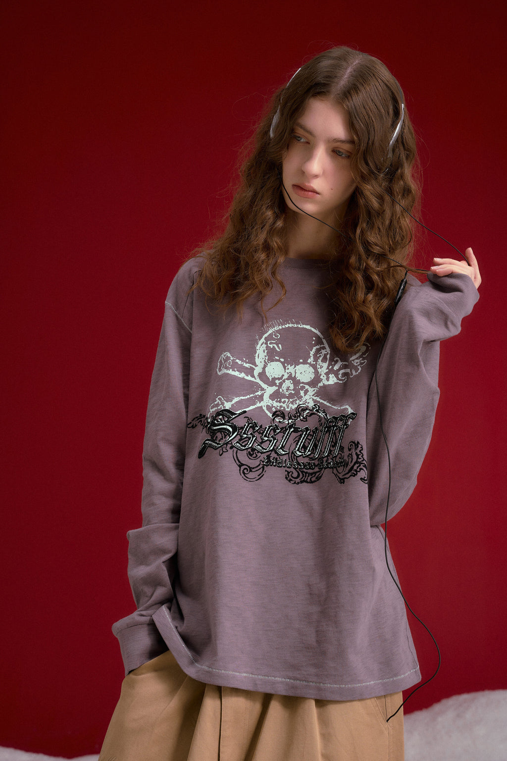 Slub Flock Skull L/S Tee in purple, a slub cotton long sleeve with a flocked skull and gothic lettering. Worn on a model, waist-up front view.