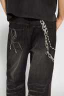 Black wash denim jeans with embroidered keychain, carabiner, and earphone charm details, and pin embroidery on ankle