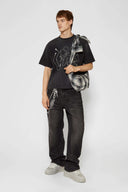 Black wash denim jeans with embroidered keychain, carabiner, and earphone charm details, and pin embroidery on ankle