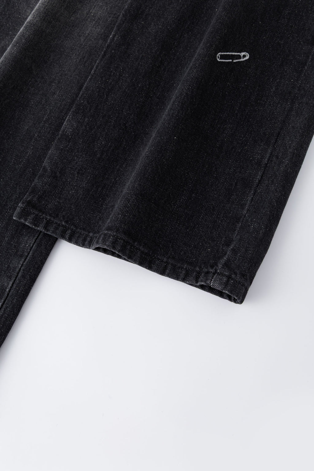 Black wash denim jeans with embroidered keychain, carabiner, and earphone charm details, and pin embroidery on ankle