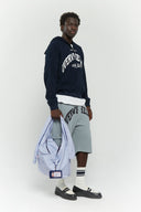 Blue striped croissant-shaped bag with shirt texture and adjustable sleeve handles for shoulder or crossbody wear, includes leather cardholder