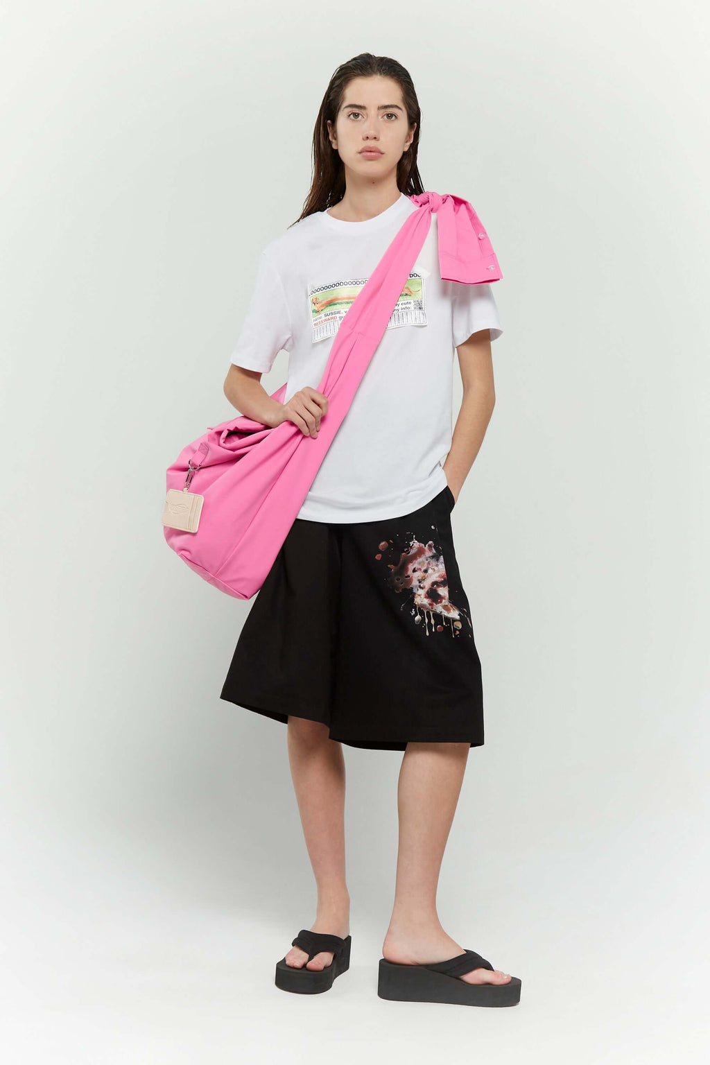 Pink croissant-shaped bag with shirt texture and adjustable sleeve handles for shoulder or crossbody wear, includes leather cardholder