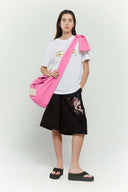 Pink croissant-shaped bag with shirt texture and adjustable sleeve handles for shoulder or crossbody wear, includes leather cardholder