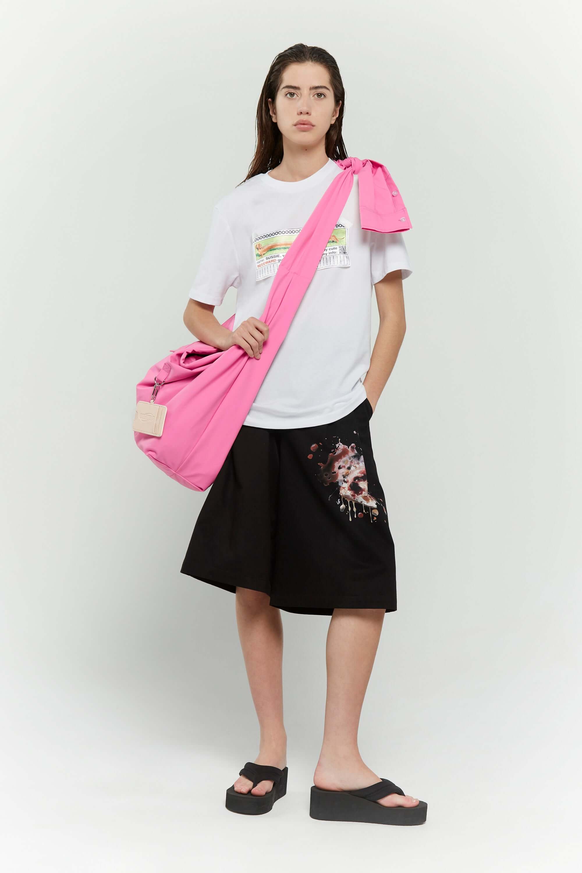 Pink croissant-shaped bag with shirt texture and adjustable sleeve handles for shoulder or crossbody wear, includes leather cardholder