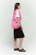 Pink croissant-shaped bag with shirt texture and adjustable sleeve handles for shoulder or crossbody wear, includes leather cardholder