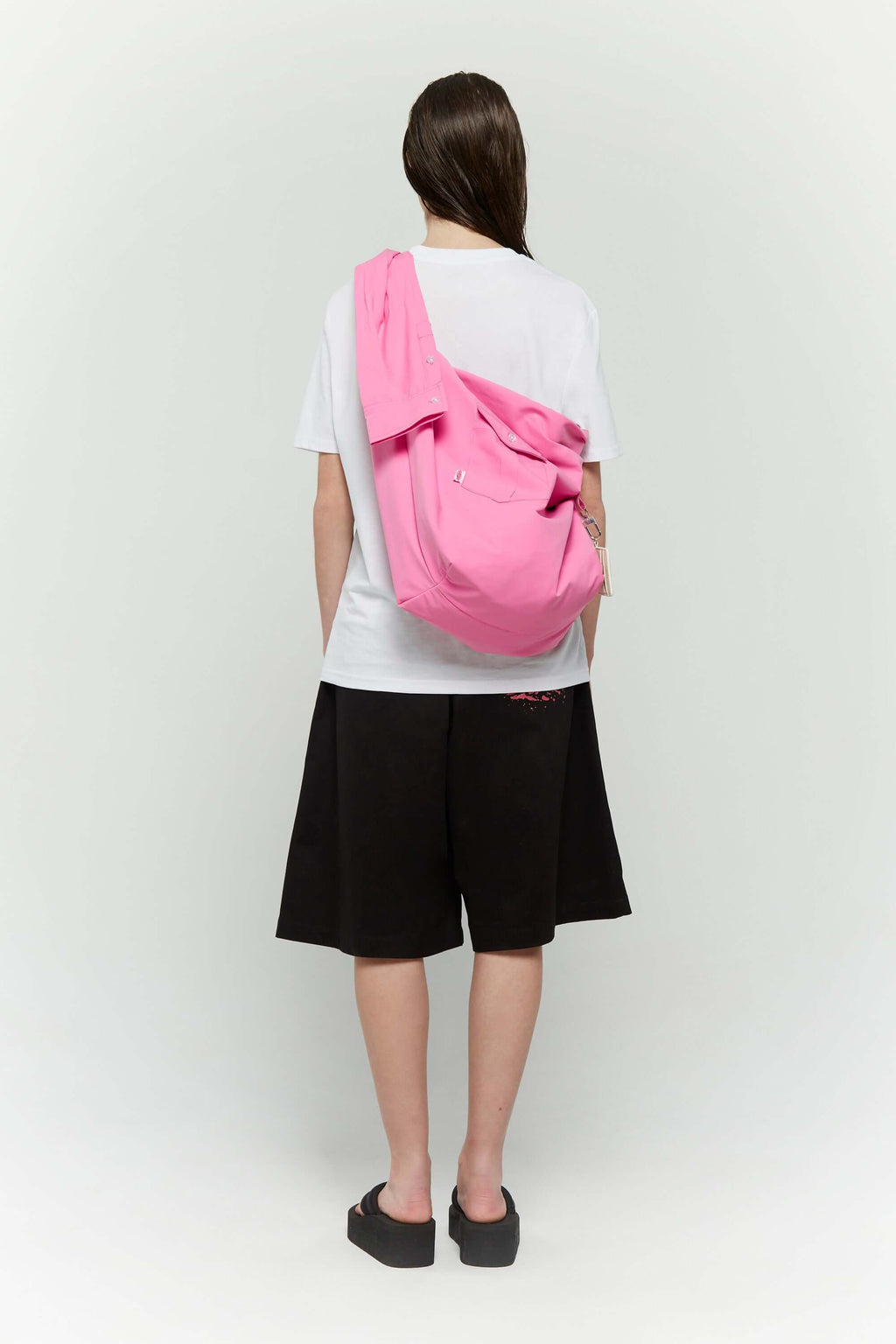 Pink croissant-shaped bag with shirt texture and adjustable sleeve handles for shoulder or crossbody wear, includes leather cardholder