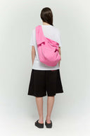 Pink croissant-shaped bag with shirt texture and adjustable sleeve handles for shoulder or crossbody wear, includes leather cardholder