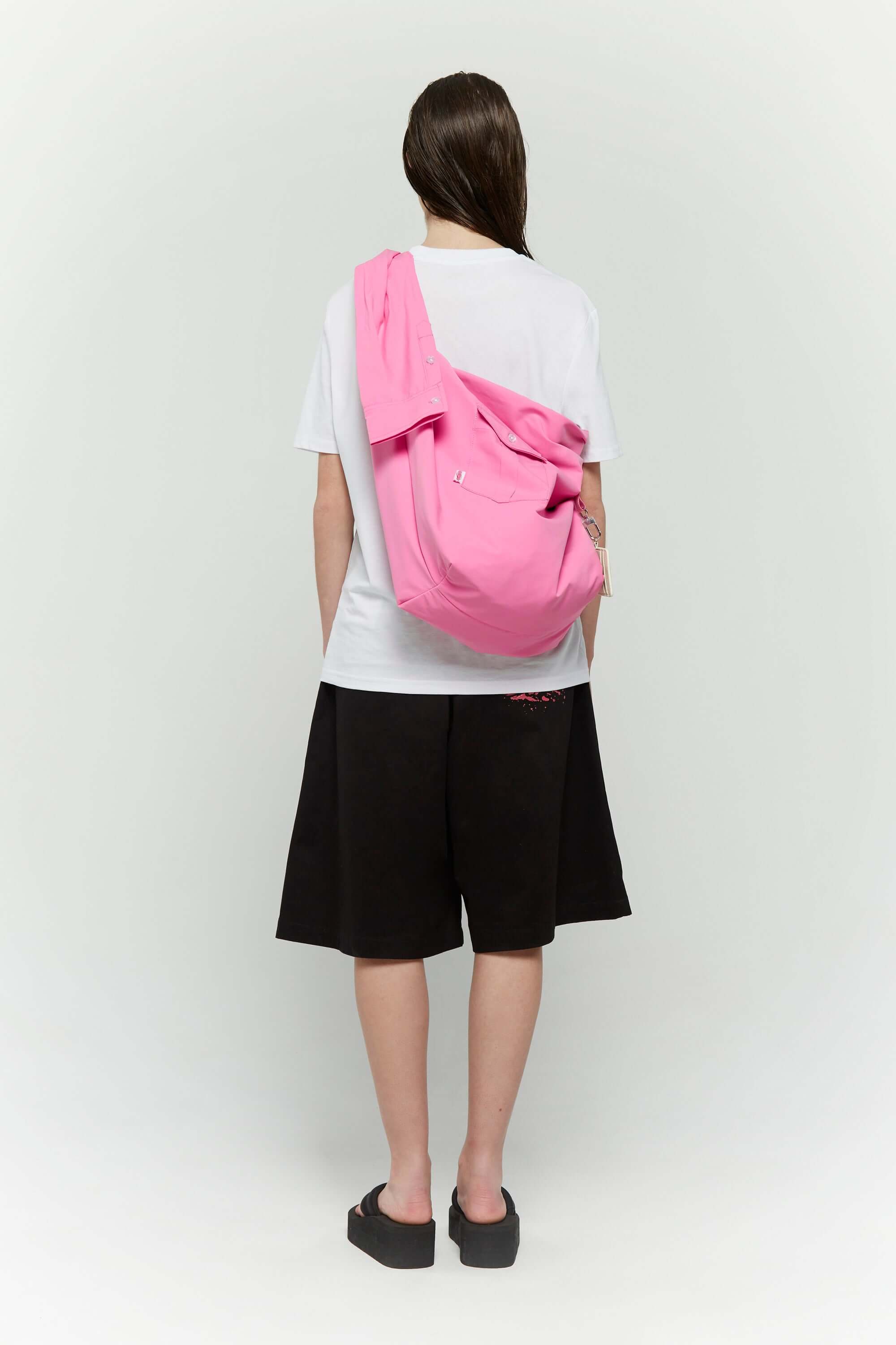 Pink croissant-shaped bag with shirt texture and adjustable sleeve handles for shoulder or crossbody wear, includes leather cardholder