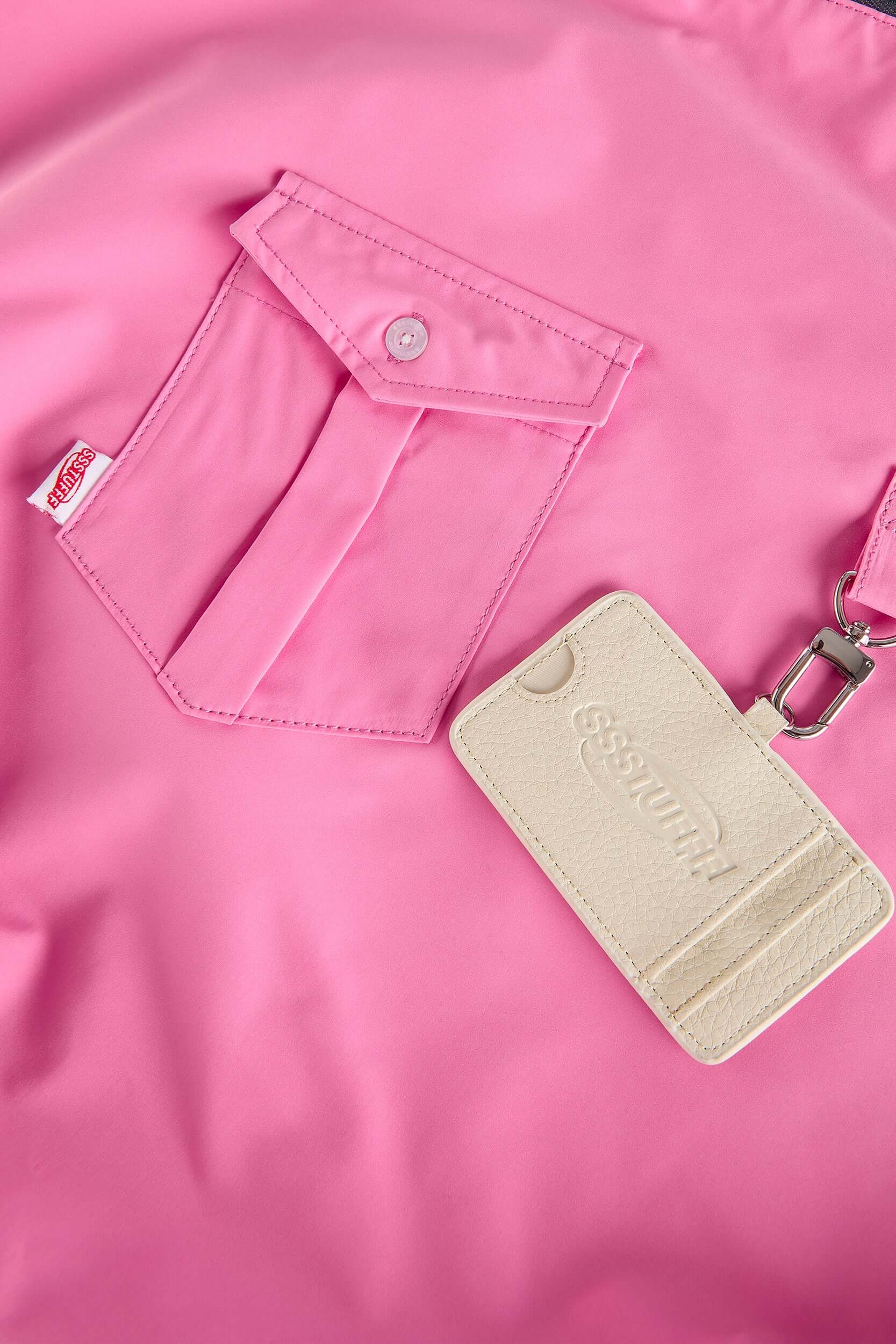 Pink croissant-shaped bag with shirt texture and adjustable sleeve handles for shoulder or crossbody wear, includes leather cardholder