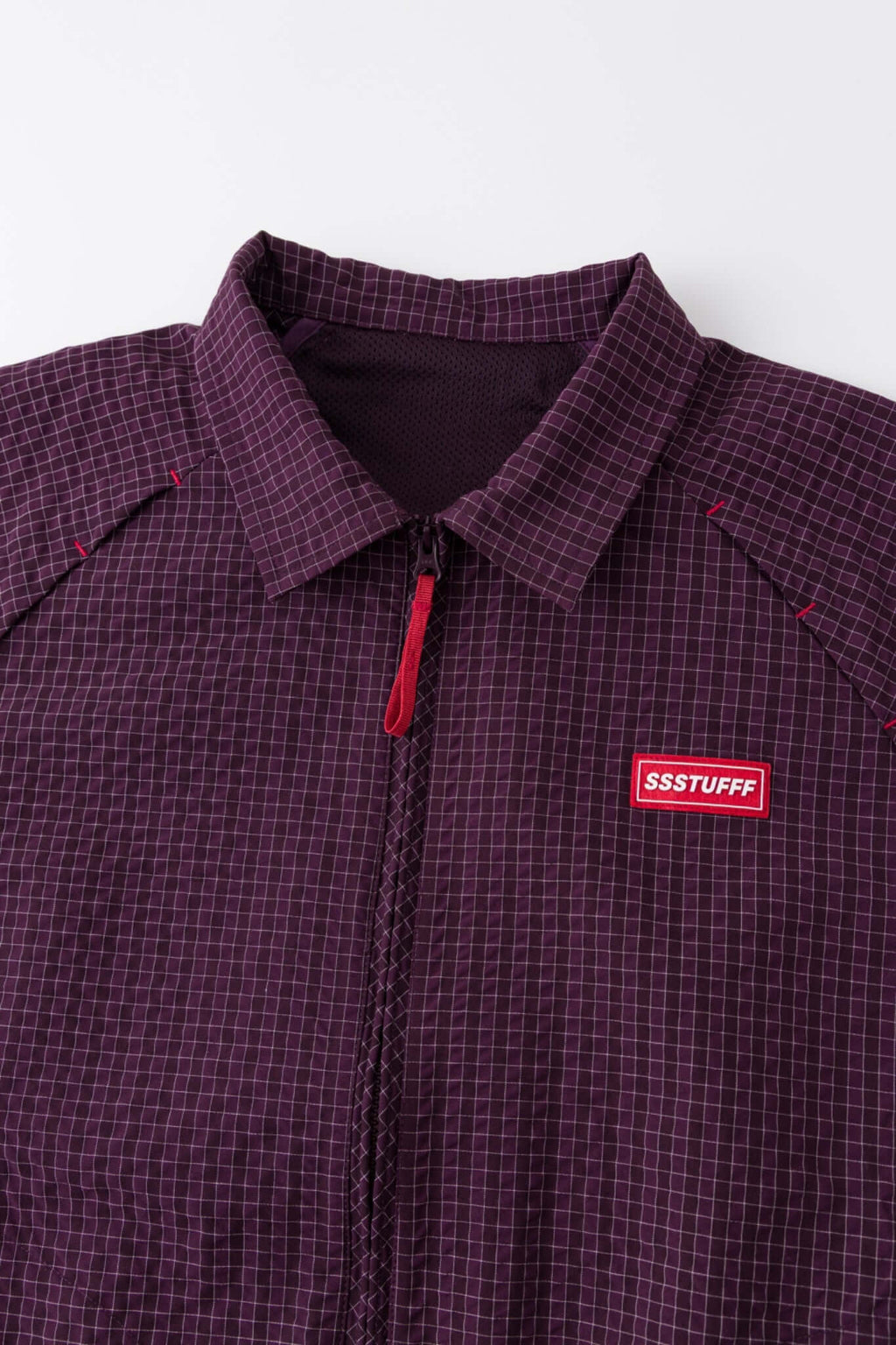 Burgundy checkered shirt with a red logo and red details in the zipper
