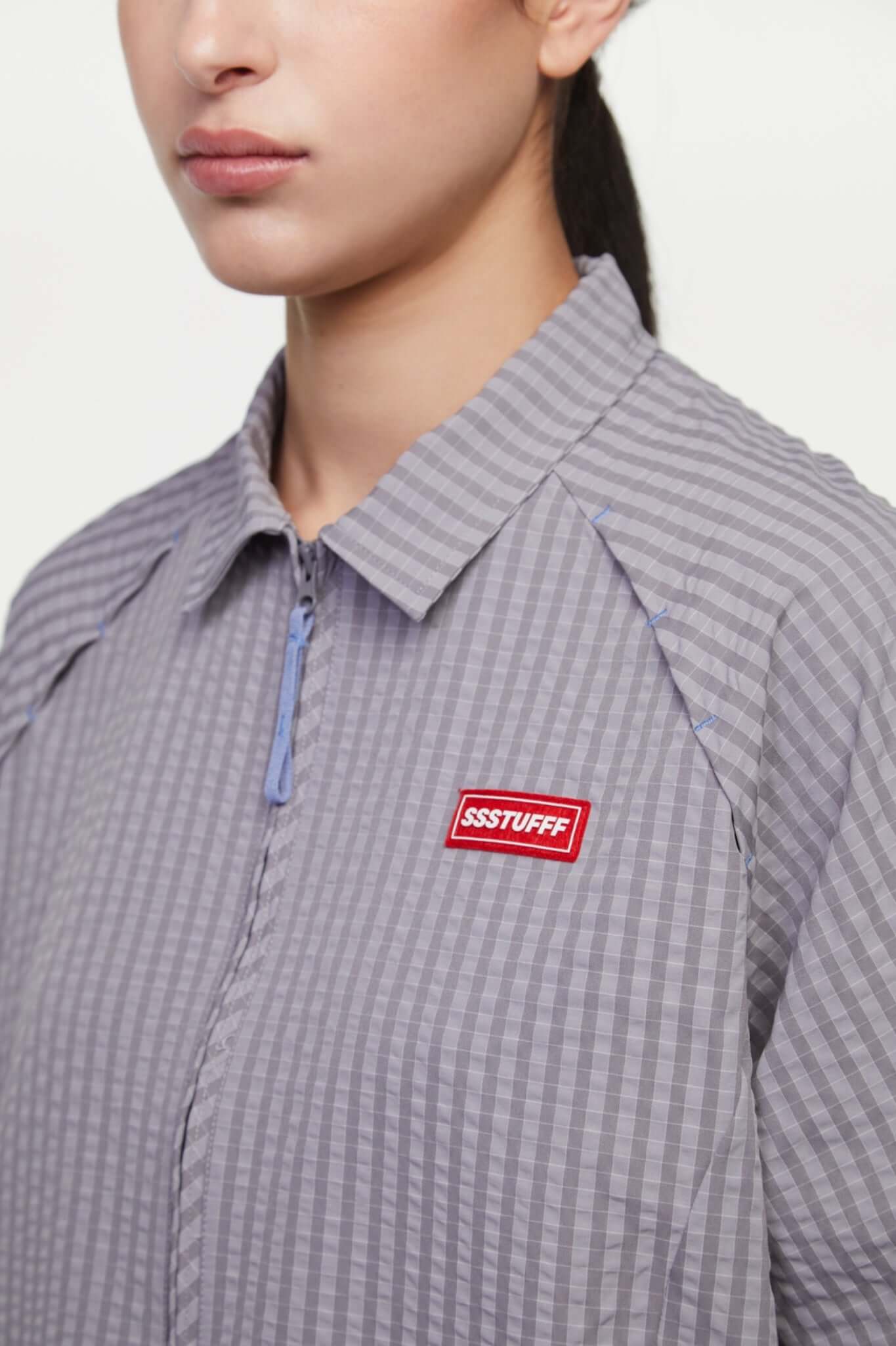 Grey checkered shirt with a red logo and red details in the zipper
