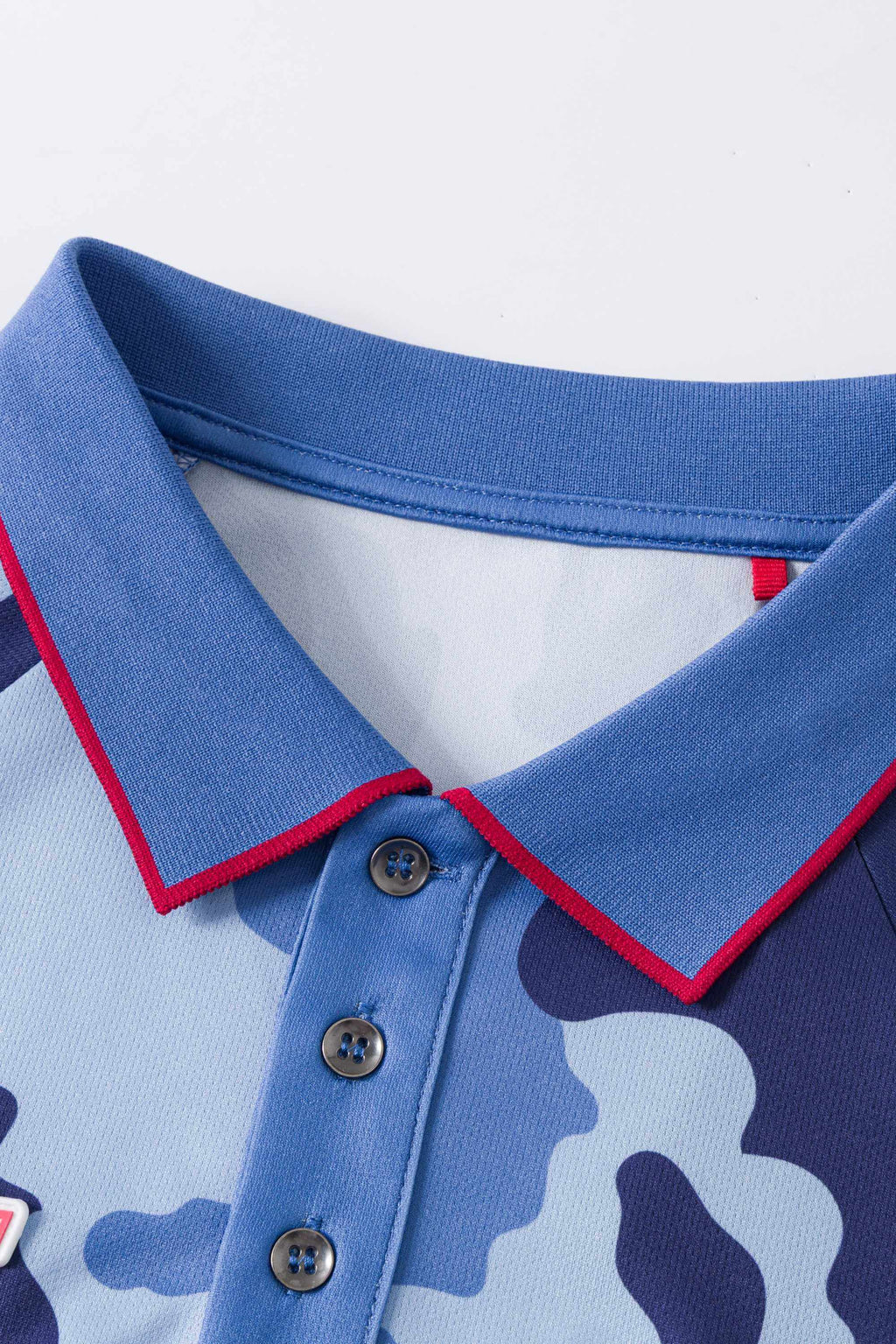 Close-up of a blue and light blue camouflage polo shirt with a red trim on a white background