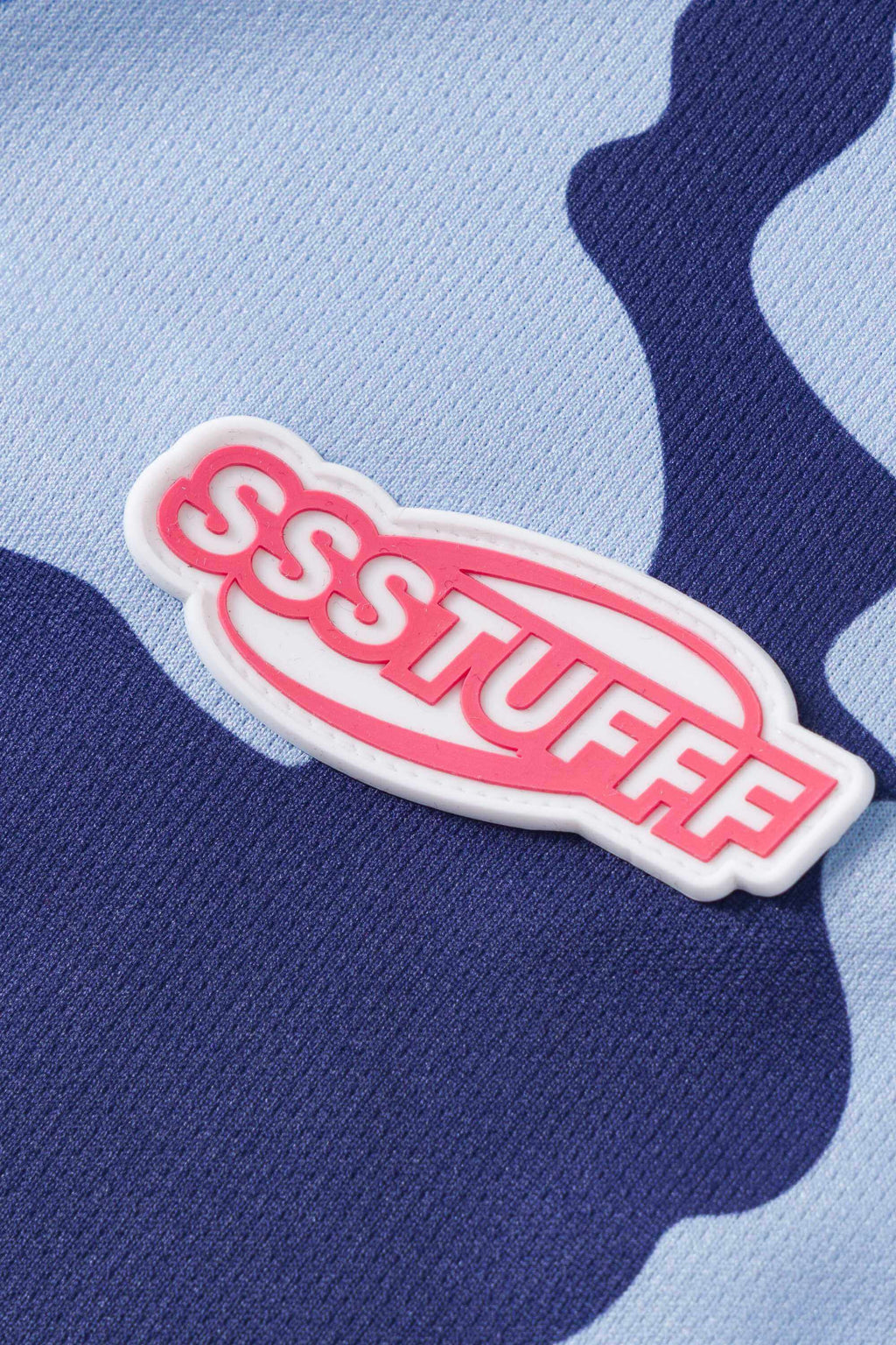 Close-up of a logo patch with 'SSSTUFFF' text on a blue and light blue camouflage jersey