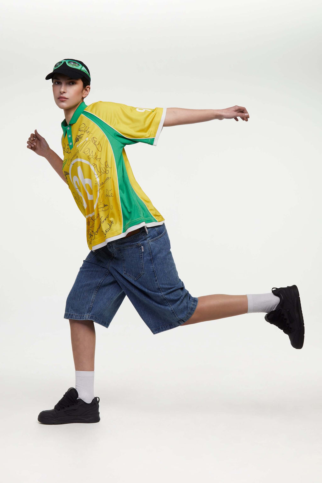 Person wearing a yellow and green sports jersey with '96' and signatures, blue shorts, and black shoes on a white background