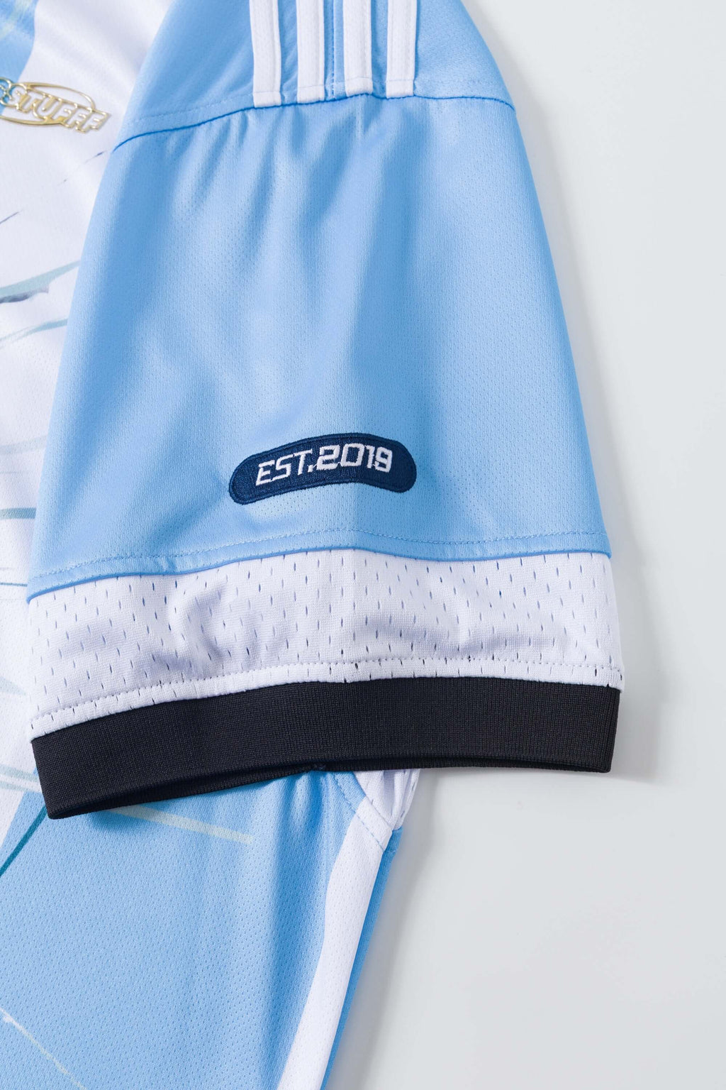 Close-up of a light blue and white sports jersey with 'EST. 2018' logo on a white background