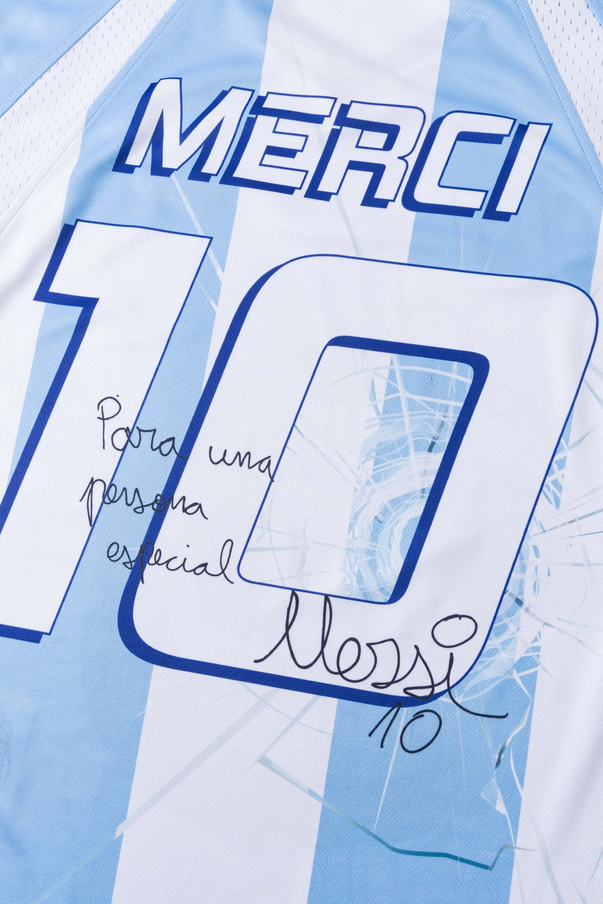Close-up of a light blue and white sports jersey signed with 'MERCI' and number '10' printed on it.
