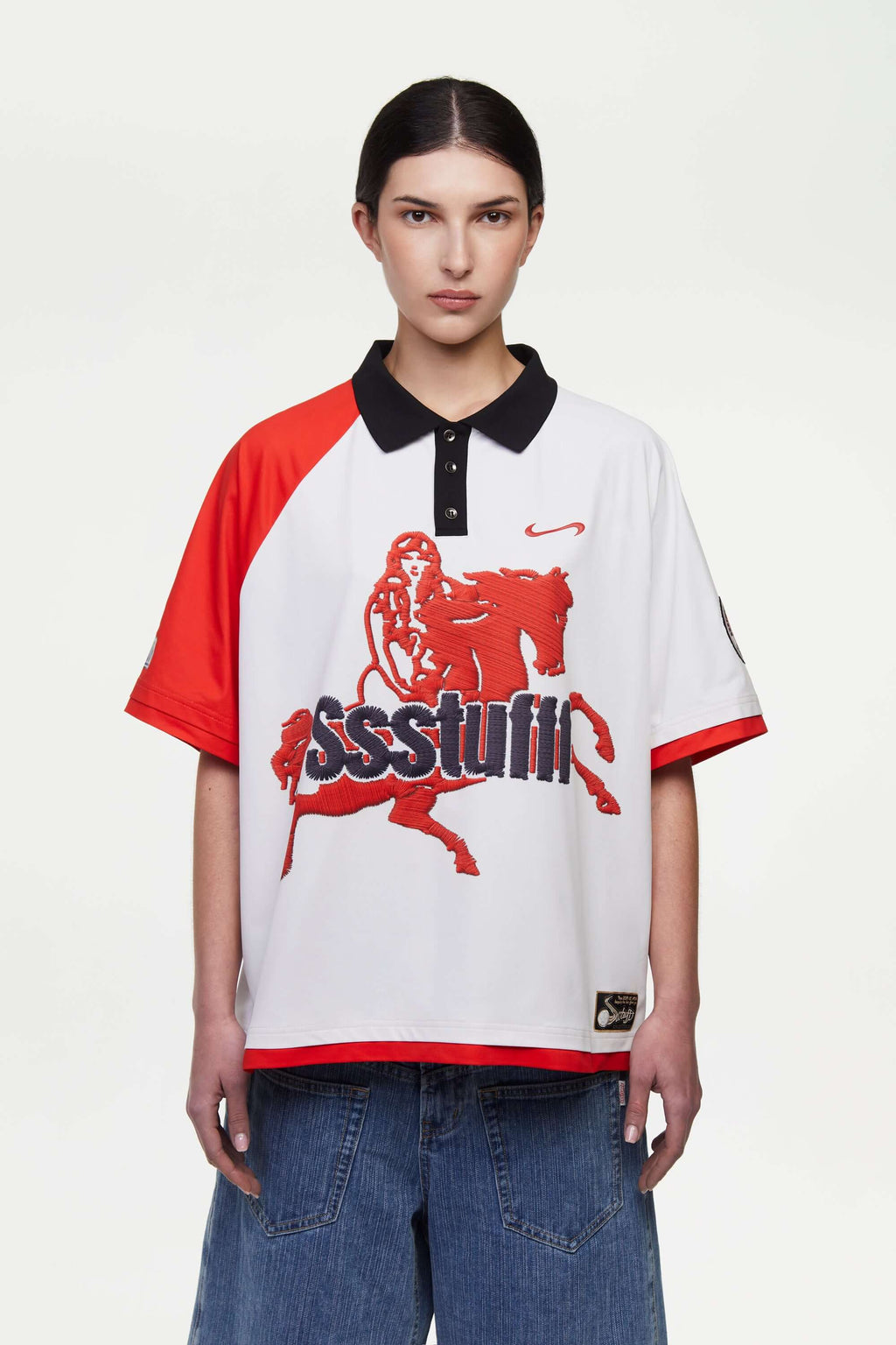 Person wearing a white football polo shirt with red accents and a print mimicking embroidered logo and motive in red and black