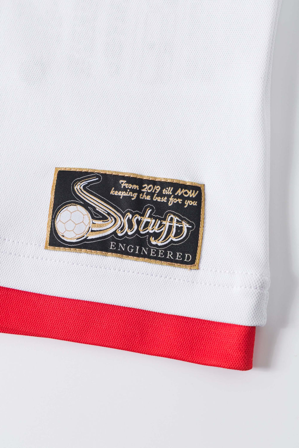 Close-up of a white shirt with a red trim and a branded patch on a white background