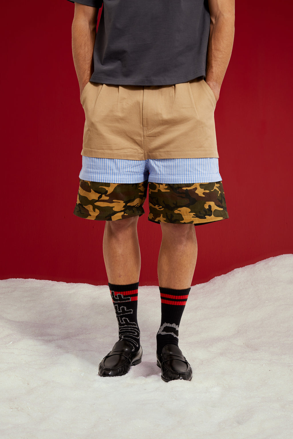 5 in 1 Layered Pants, five zip-together layers of khaki, stripe, camo and olive workwear. Worn on a model, close-up detail, zipped down to shorts length.