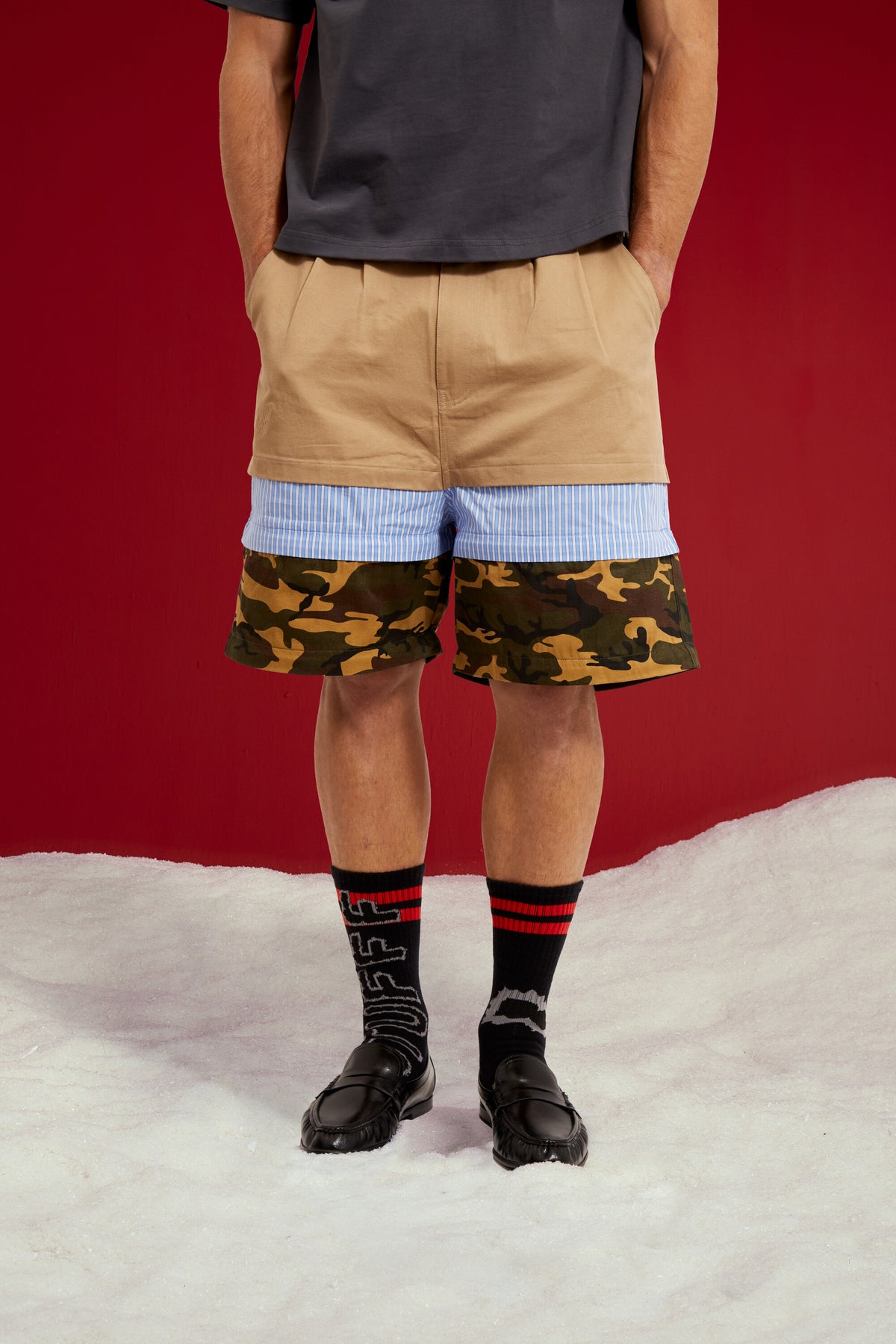 5 in 1 Layered Pants, five zip-together layers of khaki, stripe, camo and olive workwear. Worn on a model, close-up detail, zipped down to shorts length.
