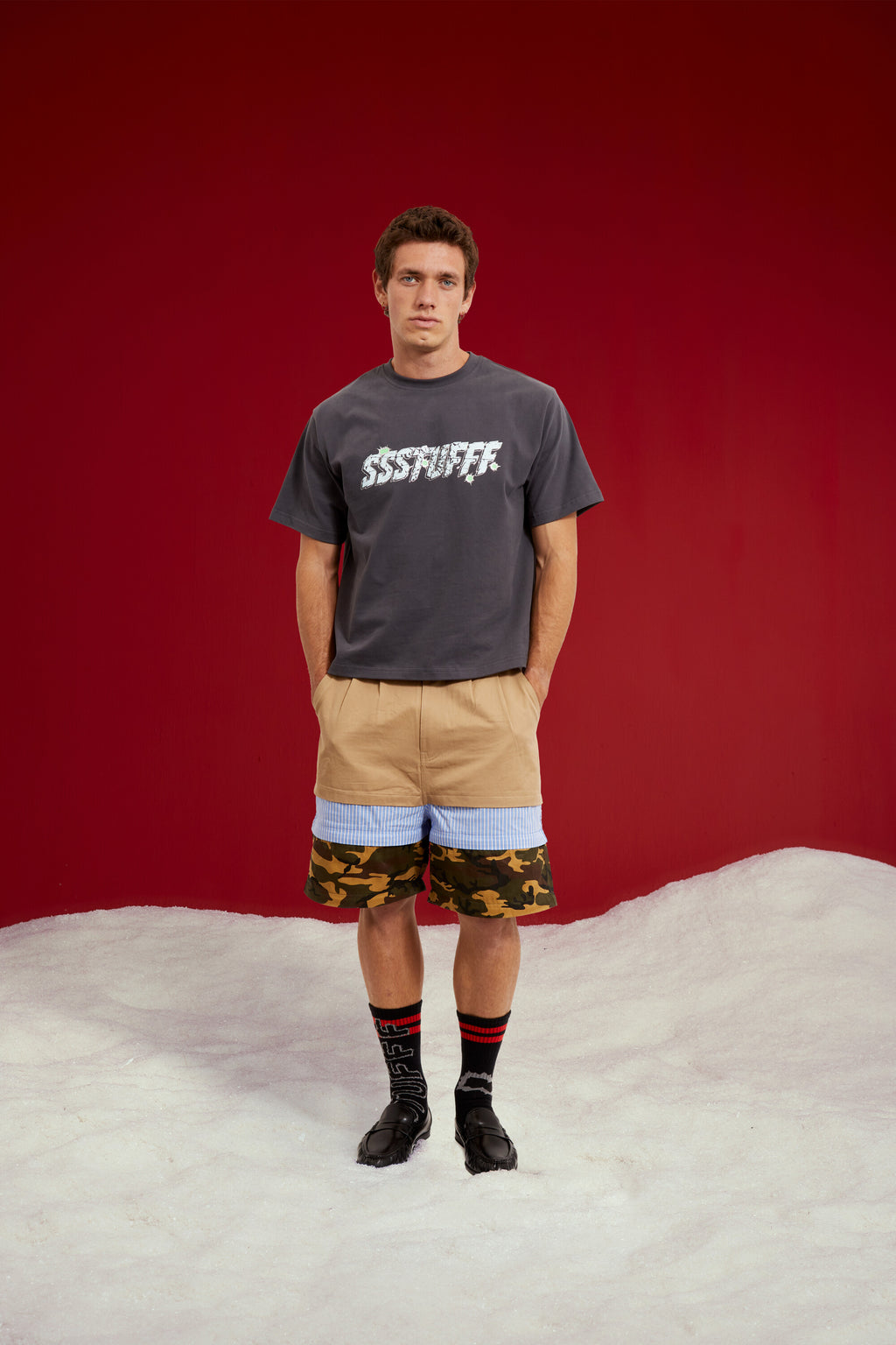 5 in 1 Layered Pants, five zip-together layers of khaki, stripe, camo and olive workwear. Worn on a model, full-length front view, zipped down to shorts length.