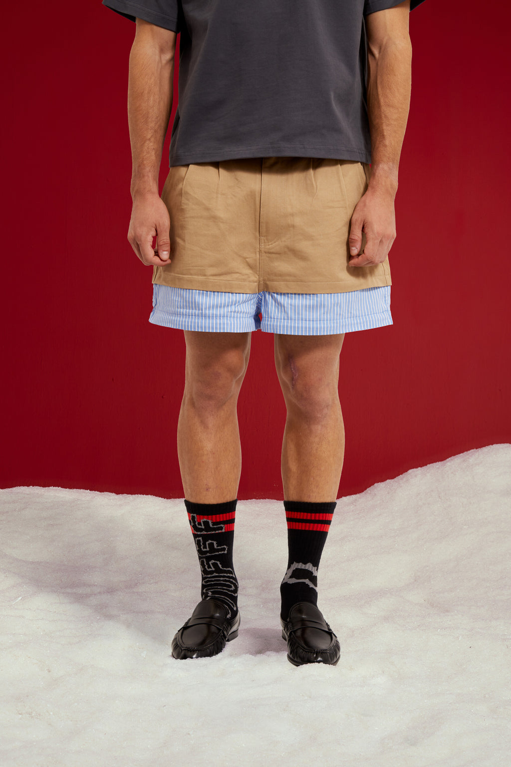 5 in 1 Layered Pants, five zip-together layers of khaki, stripe, camo and olive workwear. Worn on a model, close-up detail, zipped down to its shortest length.