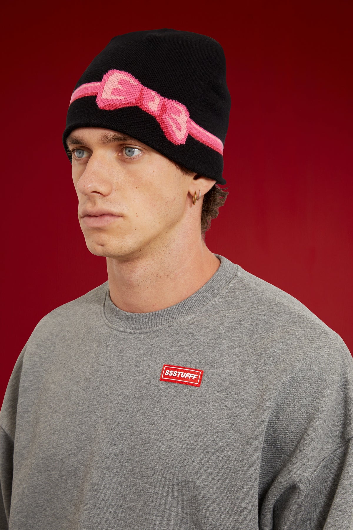 Bow Beanie in black, wrapped in pink bow tape with the bow tied at the front. Worn on a model, close-up detail, front of the cap.