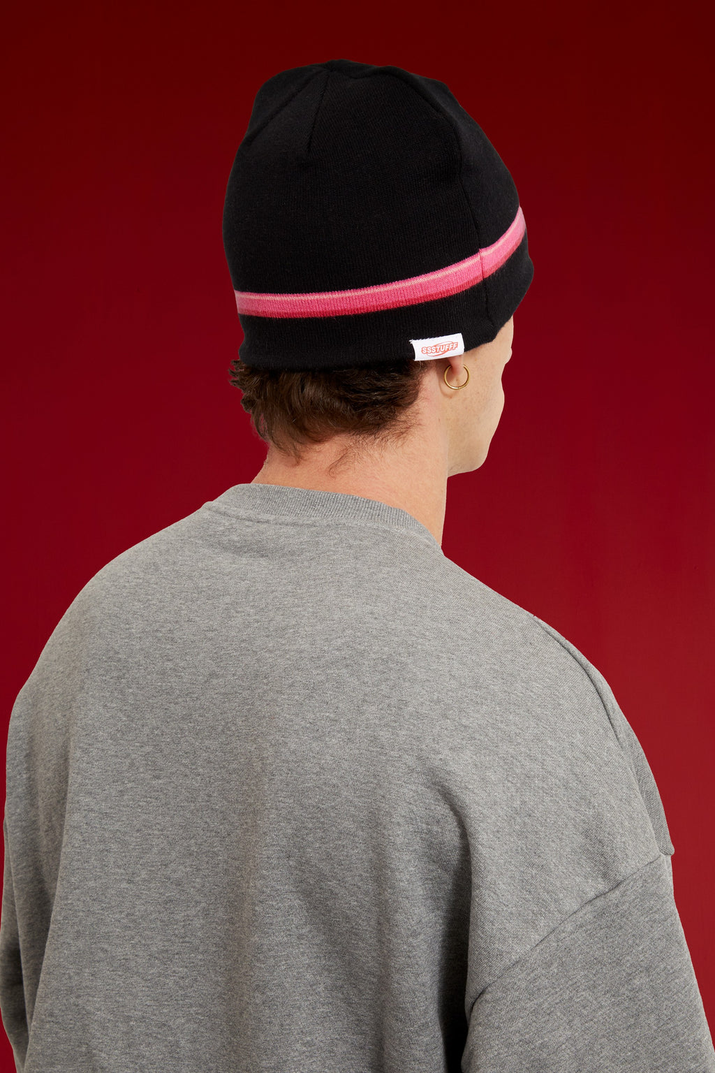 Bow Beanie in black, wrapped in pink bow tape with the bow tied at the front. Worn on a model, close-up detail, back of the cap.