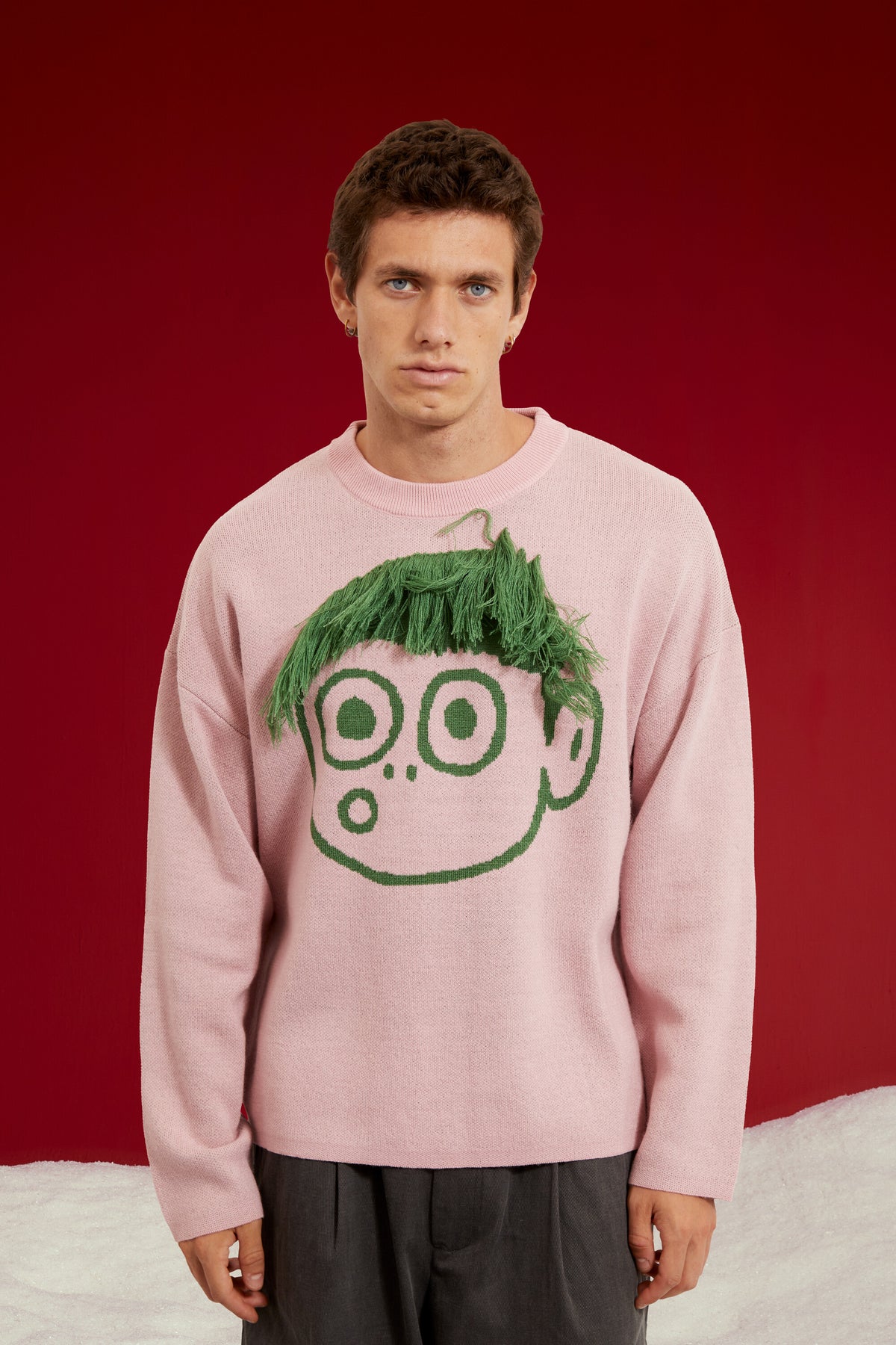 Cut My Hair Knit in pink, knitted with a character whose green fringe can be cut. Worn on a model, waist-up view, close-up of the green cuttable fringe.