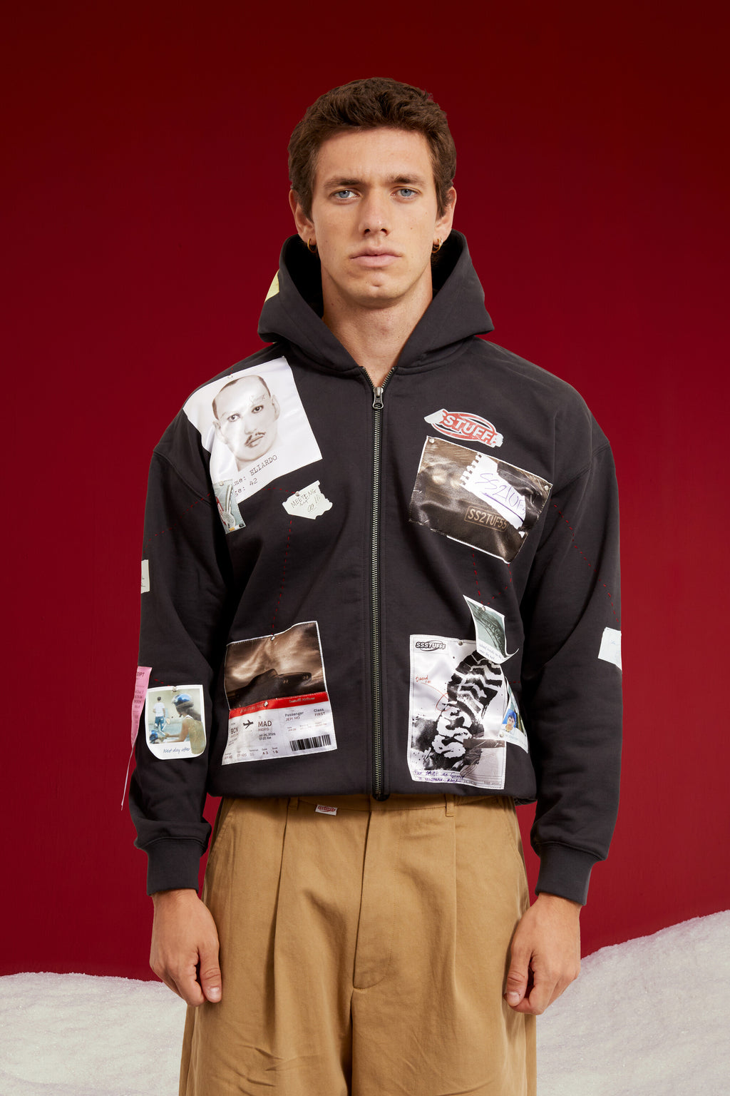 Detective Board Zip Up Hoodie in black, covered with pinned photographs and evidence patches like a detective's case board. Worn on a model, waist-up view.