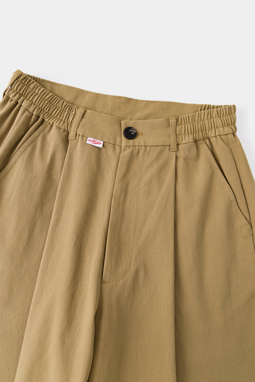 Close-up of the beige waistband, front pleats and red Ssstufff tab.