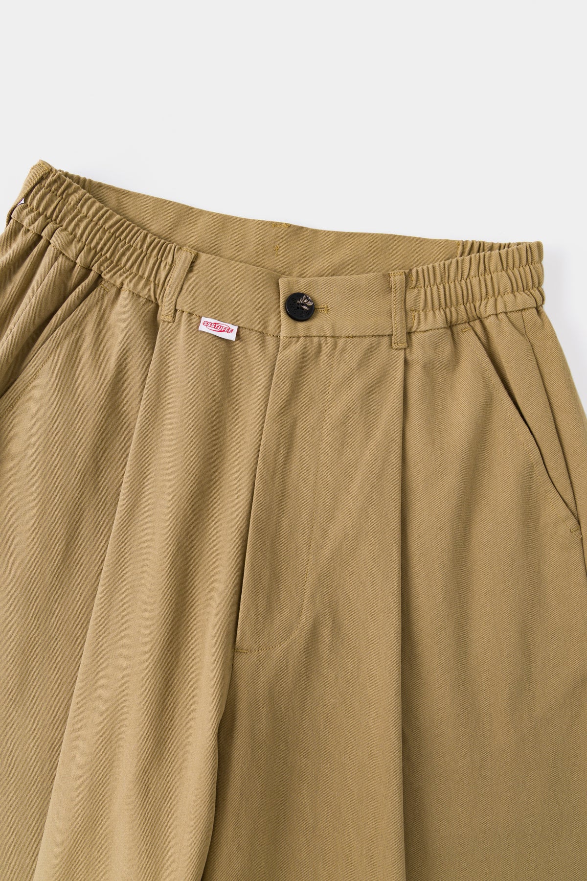 Close-up of the beige waistband, front pleats and red Ssstufff tab.