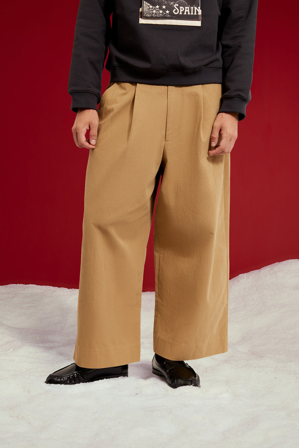 Dress Pants in beige, cut as an oversized pleated wide leg trouser. Worn on a model, close-up detail.
