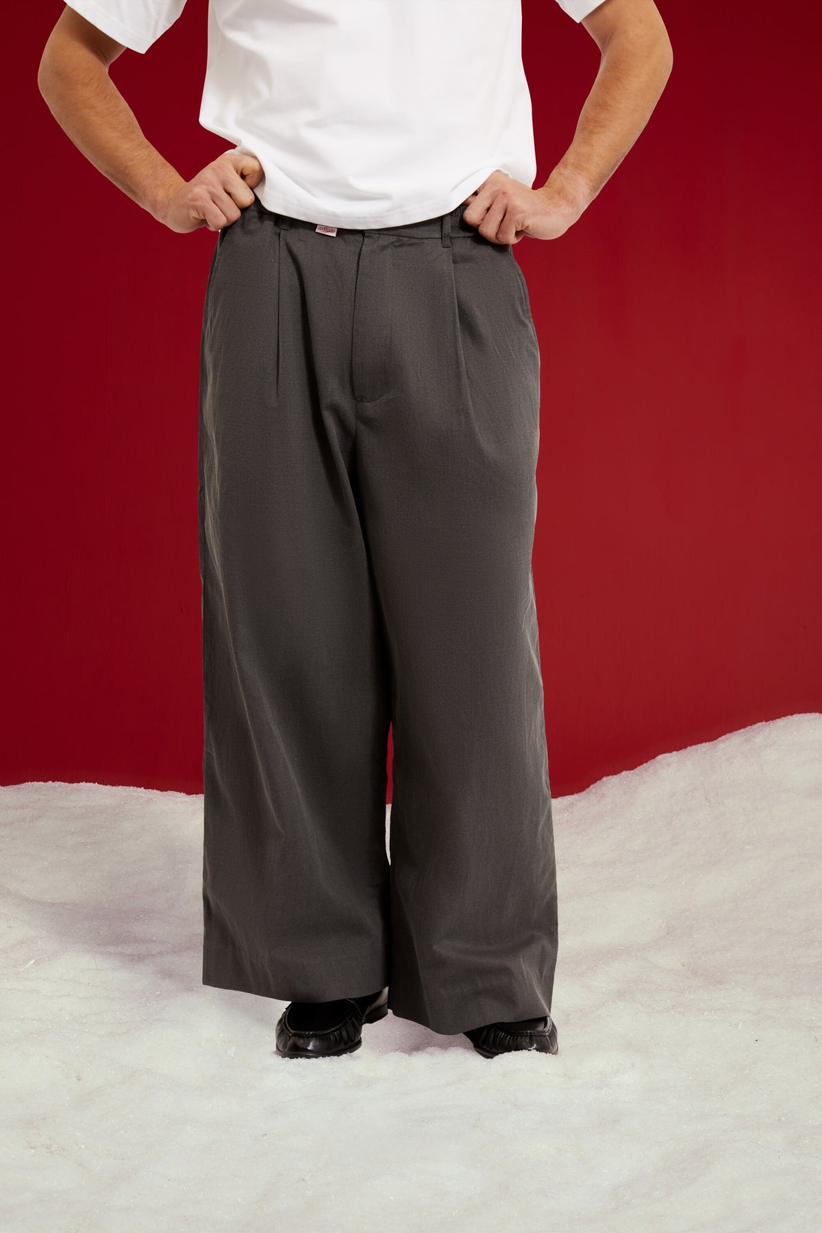 Dress Pants in dark grey, cut as an oversized pleated wide leg trouser. Worn on a model, close-up detail, front.
