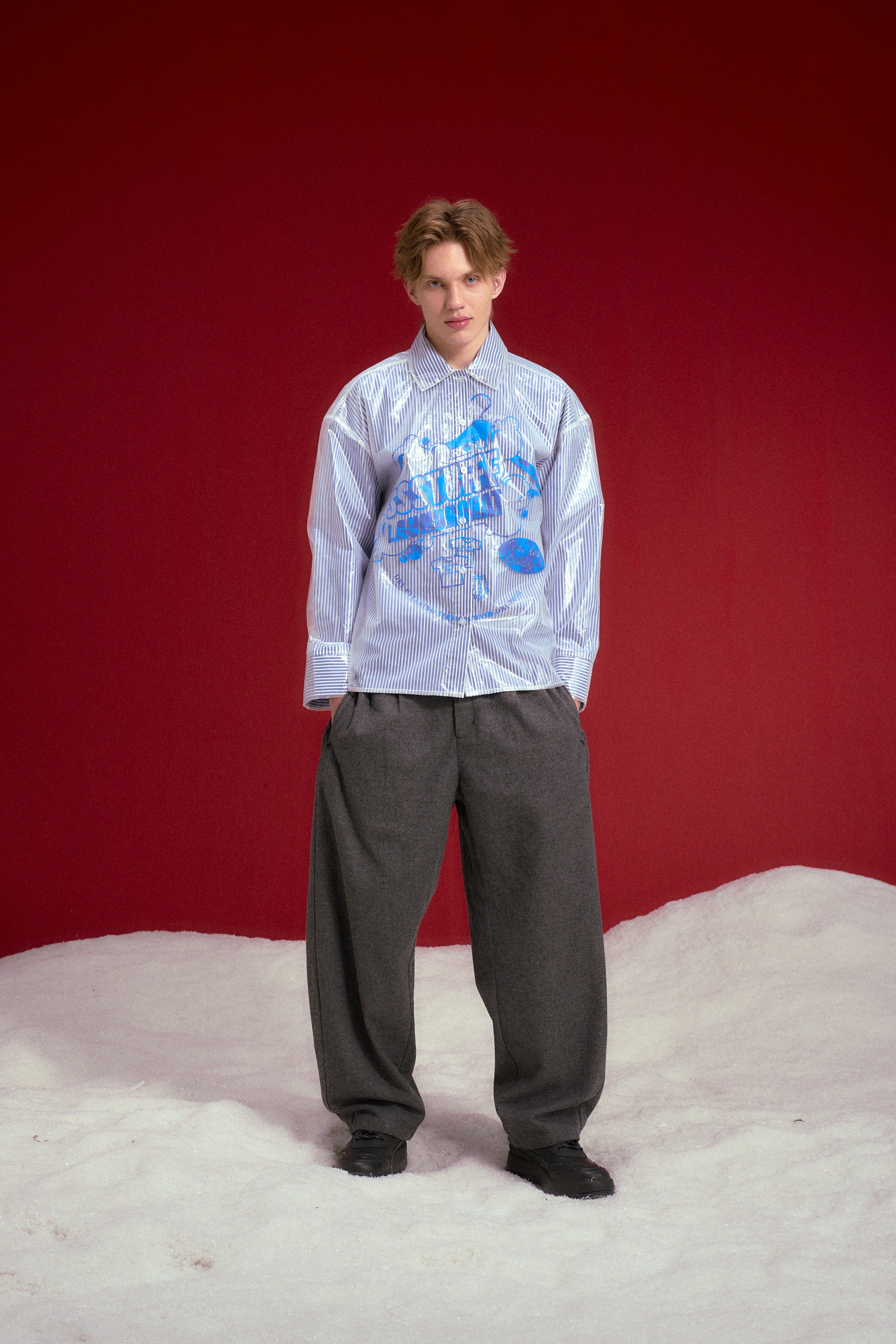 Dry Cleaned Shirt, a blue striped shirt sealed inside a printed dry cleaner's garment bag. Worn on a model, full-length front view, worn buttoned up.