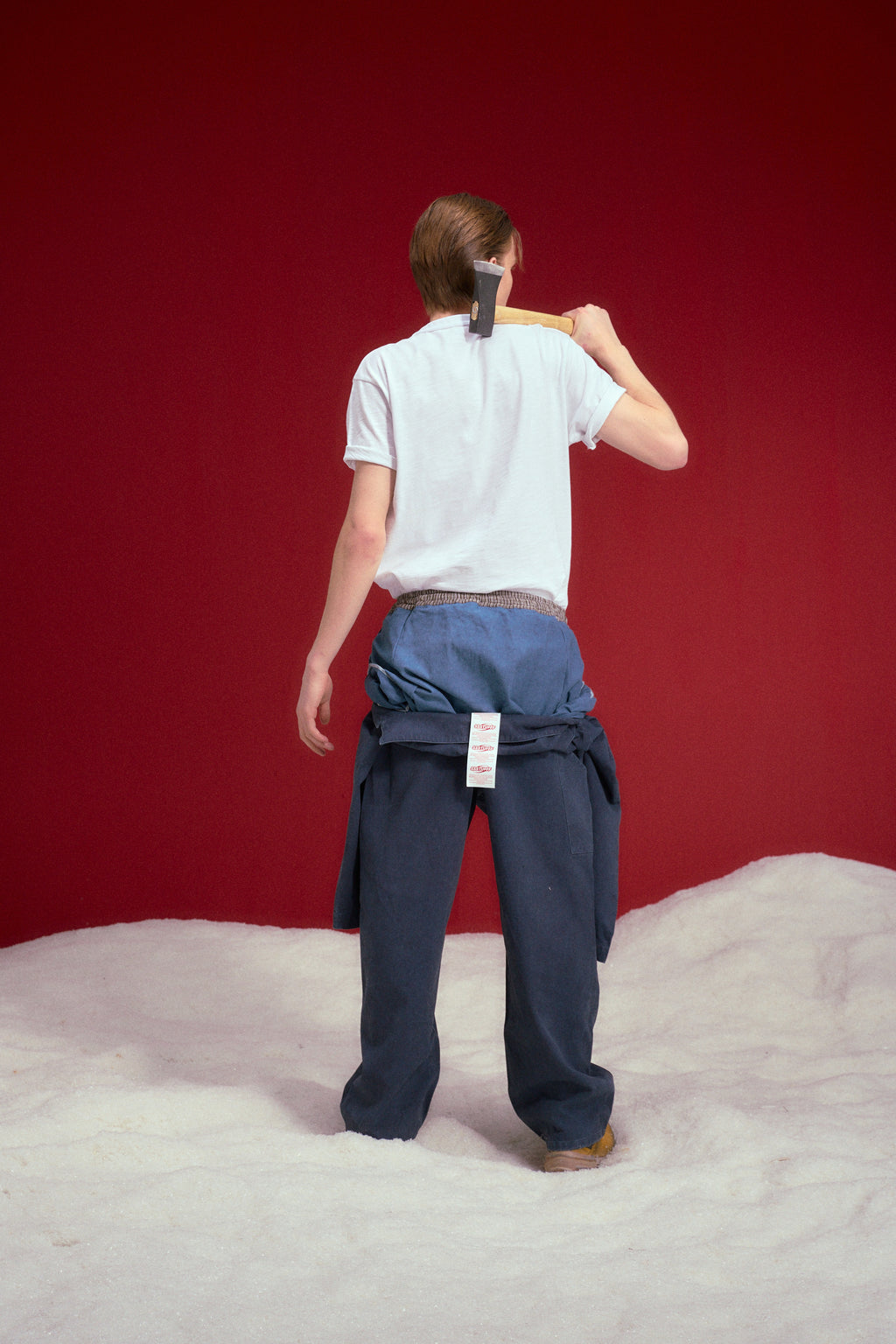 Fake Overall Pants in washed denim, with a fake overall bib and braces folded down at the waist. Worn on a model, full-length back view.