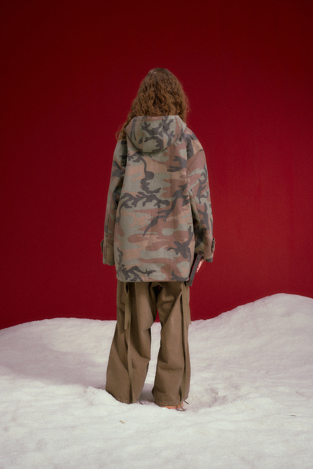 Faux Wax Camo Parka in woodland camo, with a detachable hood and multiple pockets. Worn on a model, full-length back view.