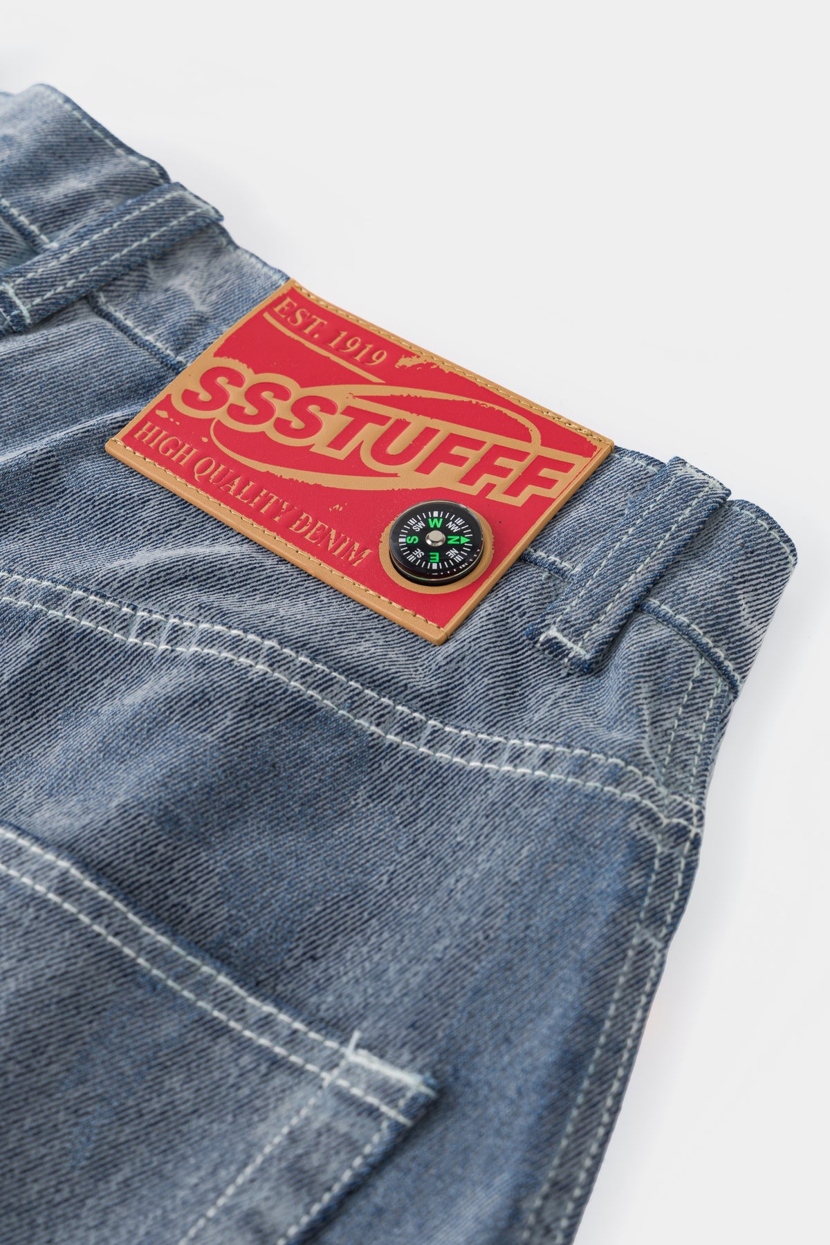 Close-up of the red SSSTUFFF Est. 1919 denim label on the flocked back waistband.