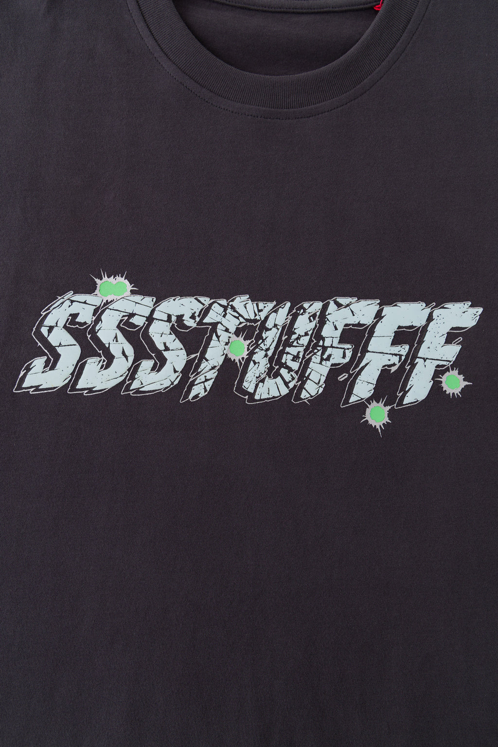 Close-up of the raised puff print SSSTUFFF shattered-glass graphic with green impact marks.