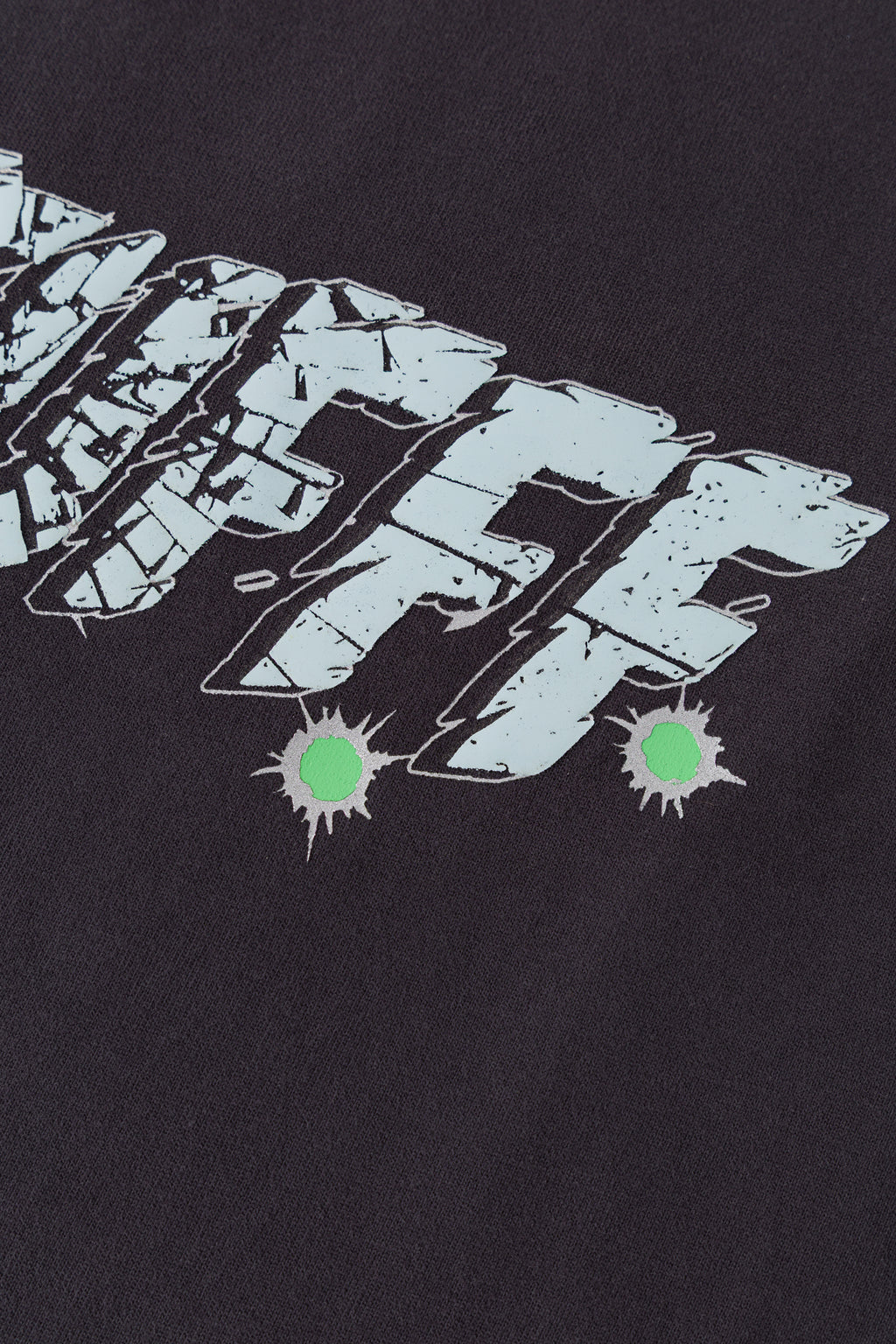 Detail of the cracked glass texture and green bullet-hole splatters on the Gunshots Tee.