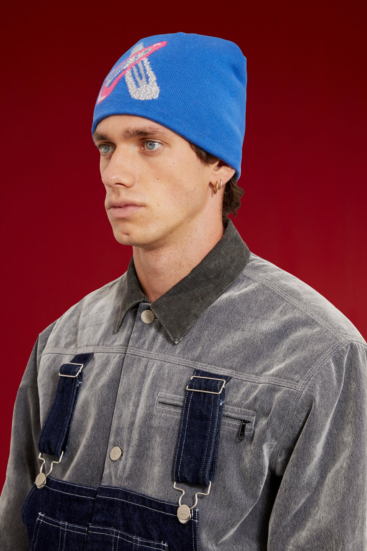 Hairclip Beanie in blue, knitted with an oversized pink and silver hair clip on the front. Worn on a model, close-up detail, front of the cap.