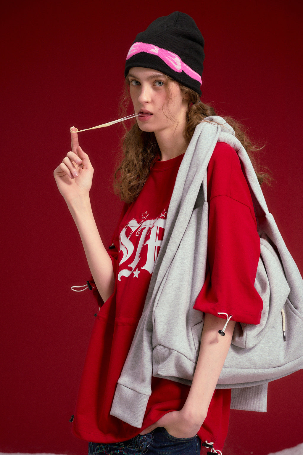 Hoodie Bag in grey marl, a hoodie rebuilt as a crossbody bag with the two sleeves knotted into the strap. Worn on a model, waist-up view.