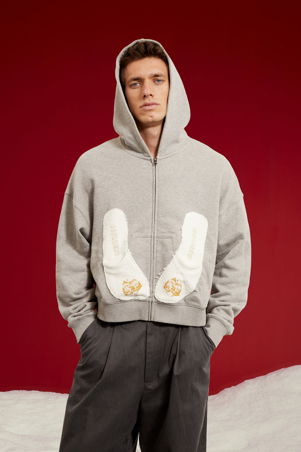 Hotel Slipers Pocket Zip Up Hoodie in grey marl, with a pair of hotel slippers tucked into the front pocket. Worn on a model, waist-up view.