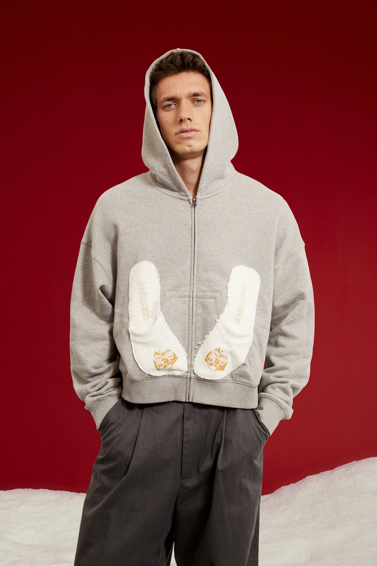 Hotel Slipers Pocket Zip Up Hoodie in grey marl, with a pair of hotel slippers tucked into the front pocket. Worn on a model, waist-up view.