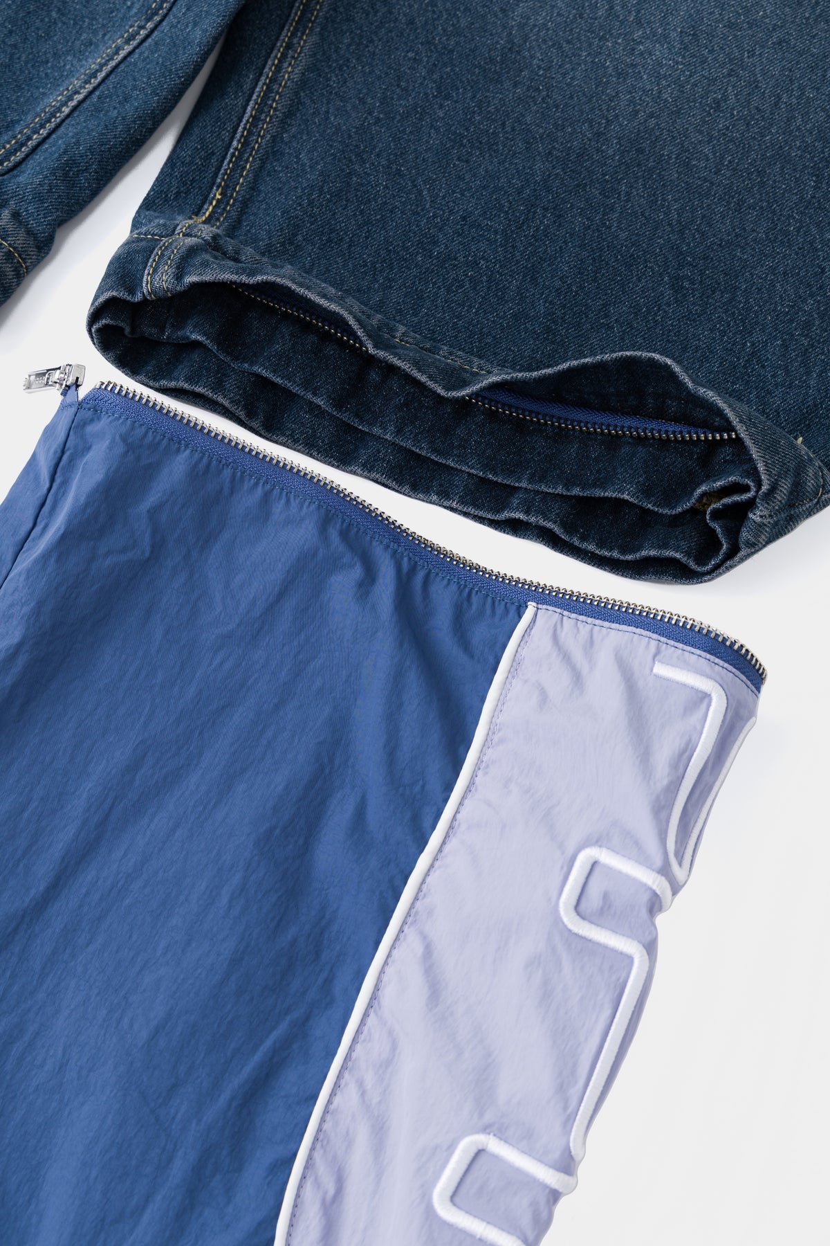 Close-up of the zip at the knee that joins the denim shorts to the nylon track legs.