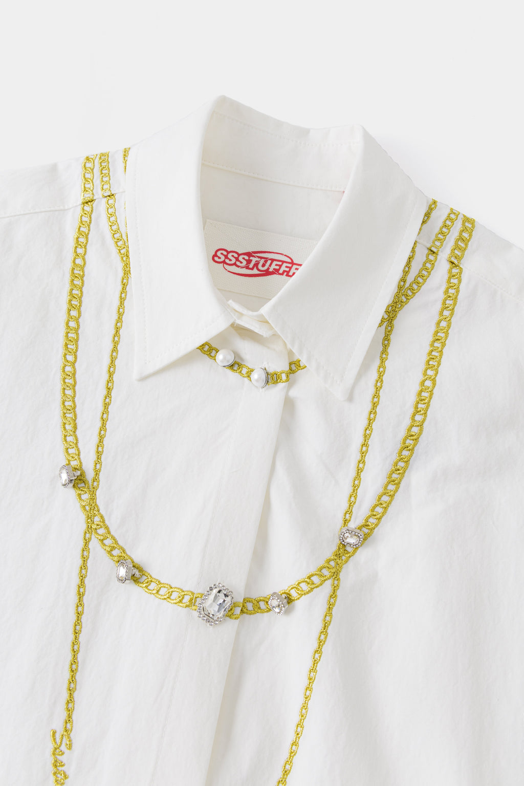 Close-up of the collar and layered embroidered gold chains, with pearls at the neck and a crystal pendant.