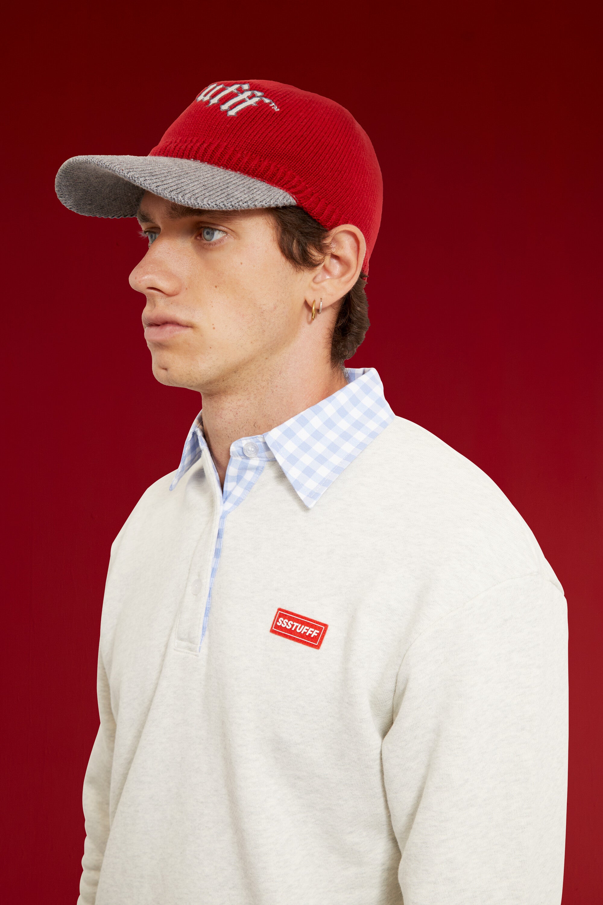 Red Knitted Cap with a contrast grey knitted brim and gothic ssstufff embroidery at the front. Worn on a model, waist-up view.
